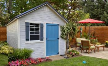 Light gray Signature Garden Shed with white trim, dark blue shutters, and a bright blue door with a ramp.